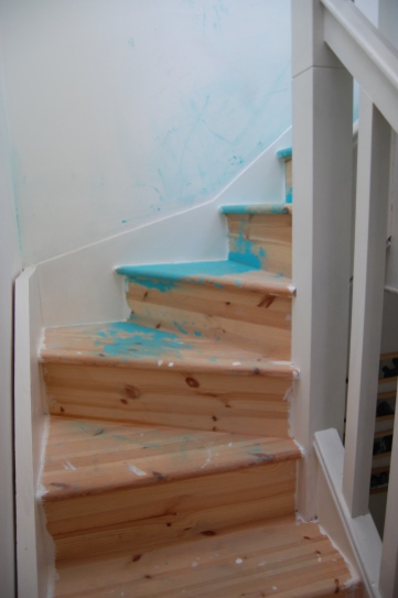 Bare wooden winding stairs, splashed with turquoise paint.